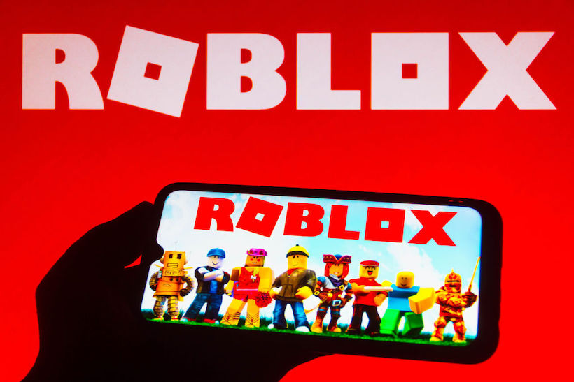 Hand holding smart phone displaying Roblox screen