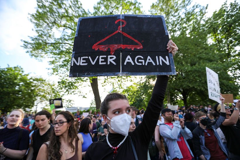 Abortion rights demonstrator holding a protest sign featuring a bloody coat hanger and the words "NEVER AGAIN"