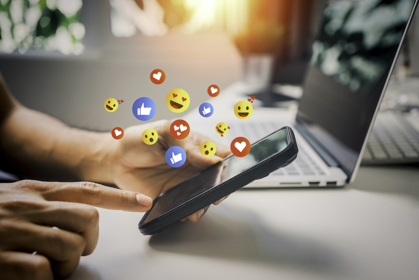 Hand touching smartphone screen with many emoji
