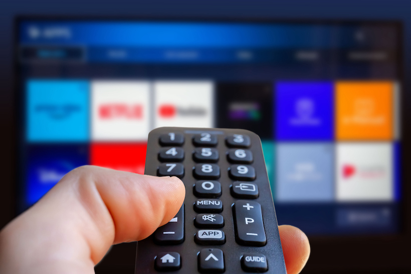 Hand holding remote control pointed at TV screen
