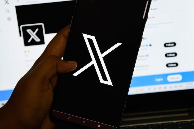 Hand holding smart phone displaying X Corp screen