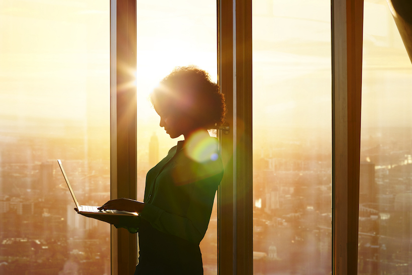 Businesswoman on laptop at window in morning sun