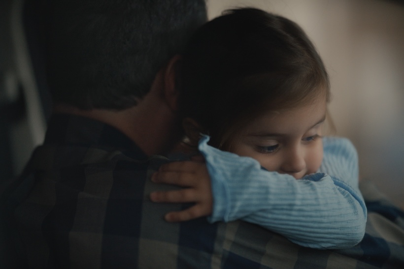 A child with her arm wrapped around her father's neck