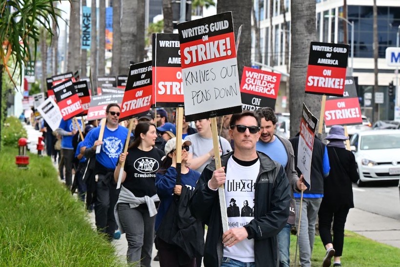 Striking WGA members carrying signs reading "Writers Guild of America On Strike"
