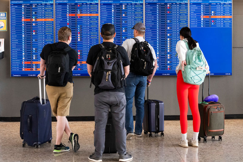 Passengers look at a flight information board showing multiple delays caused by the CrowdStrike outage