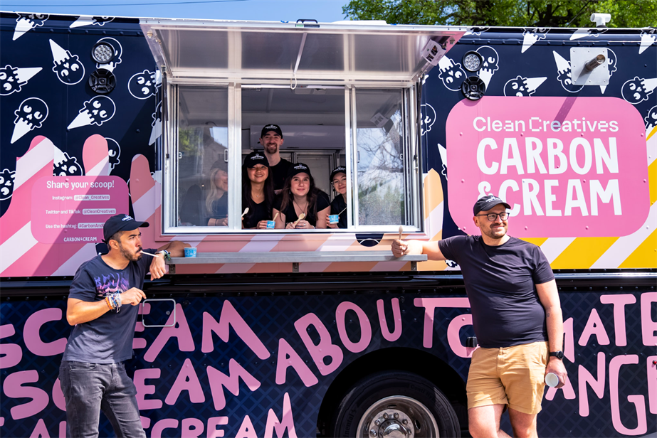 Joe Cole and Duncan Meisel stand in front of the fossil-fuel themed ice cream truck at SXSW 2023, while five people hold ice cream in the window