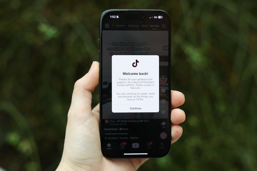 Hand holding smart phone displaying TikTok app with message regarding its ban and restoration of service