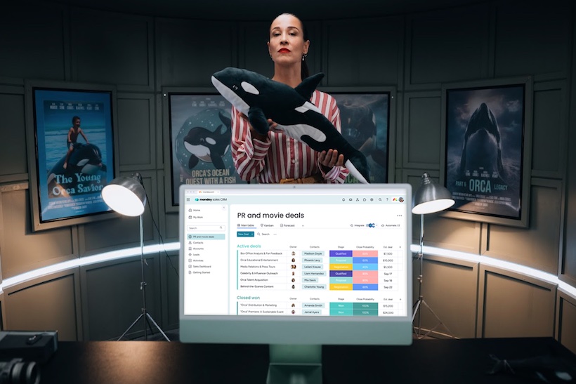 Woman holding model of orca whale standing behind an iMac computer displaying Monday.com website