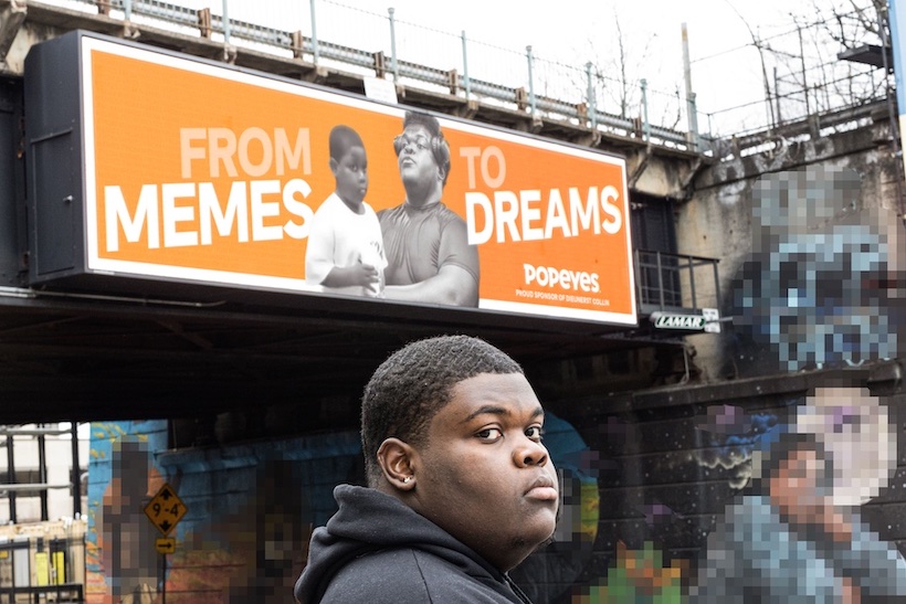 Popeyes meme kid Dieunerst Collin stands in front of a billboard featuring himself