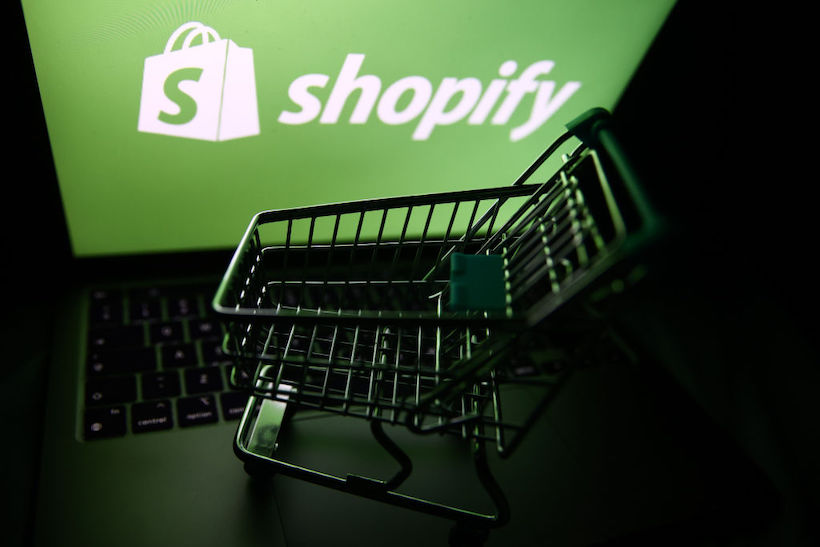 Shopify logo displayed on a laptop screen and a small shopping cart