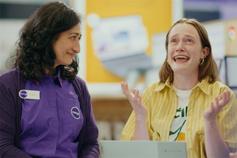 A Currys employee smiling at a customer (another woman) rejoicing over a new laptop 