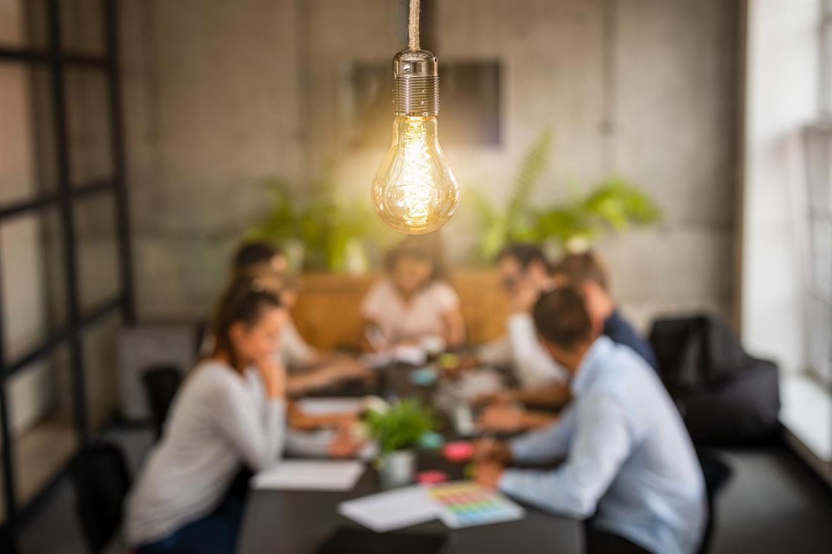 Lightbulb with background of people working at a large desk