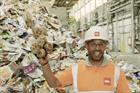 A man with a hard hat and goggles standing in front of a pile of recycling holding up a cuddly toy