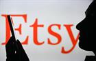 Profile of person holding smartphone with Etsy logo in background