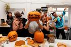 People in a kitchen holding pumpkins and signs saying 'Eat your pumpkin', some of them in 'zombie' poses