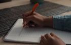 Person writing note on paper pad with orange pen