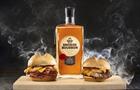 Two Arby's burgers next to bottle of smoked bourbon