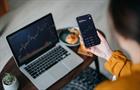 Over the shoulder view of Asian woman holding smartphone, analyzing investment trading data on crypto graph with smartphone and laptop while working at home. Cryptocurrency, bitcoin, digital ledger - stock photo