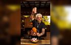 Guy Fieri pours flavortown sauce on a chicken wing held above a display of Revlon products