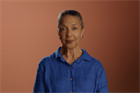 An older woman wearing a blue shirt, with her hair tied back