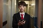 A teenage boy in a school uniform holding a mobile phone