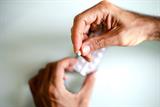 Close up of man's hands holding a pill with a pill packet in the background