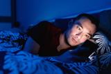 A man lying in bed at night looking at his phone