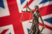 Statue of Lady Justice in front of the UK flag