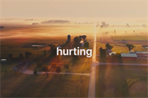 A still from the ad featuring a sunset over farmland and the word 'hurting'.