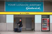 A woman stands under a sign at London Gatwick, which reads: "Your London airport Gatwick".