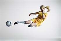 A female footballer pictured enacting a bicycle kick with a football in a plain studio