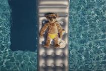 A teddy bear lying on an inflatable mattress in a swimming pool