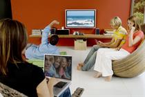 Members of family watching TV while using laptops and smartphones in a lounge room. Photo: Getty Images