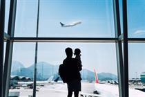 A parent and child look out of the airport terminal window as a plane takes flight 