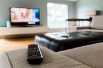 A remote control pictured with a TV in the background. (Photo: Getty Images)