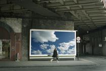 A woman walks past a billboard under a train track in the city