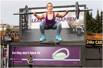 Billboard of woman squatting while weightlifting with real liquid dripping from between her legs