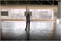Woman stands in a bright warehouse space looking at two sketches of her face 
