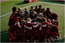 Children huddle in a circle on a football pitch