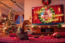 A child-dog sits in her living room, which is decked out in Christmas decorations, in front of a Sky Glass TV