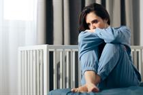 Sad woman sitting on bed next to empty crib, miscarriage concept