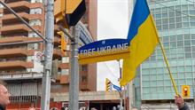 People waving Ukrainian flag in front of street sign reading "Free Ukraine"