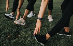 Three pairs of feet in trainers visible with people's hands reaching down to touch the toes