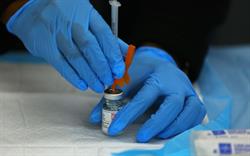 A person with blue-gloved hands uses a syringe to extract a dose of the Moderna COVID-19 vaccine from a vial.