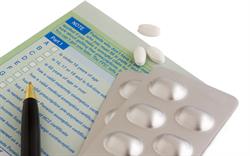 Close up image of the back of a prescription with a pen and blister pack of tablets and a few loose tablets lying on top of it