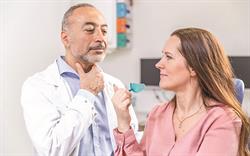 Male clinician in white coat showing female patient how to use IQoro device.