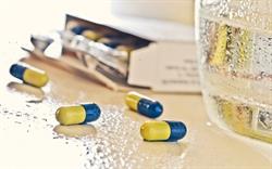Blue-yellow capsules next to a glass of water