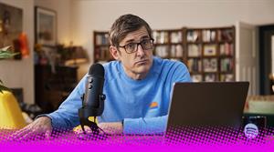 A photograph of Louis Theroux sat in front of a laptop and microphone