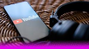 Photograph of a pair of headphones next to a smartphone showing YouTube logo