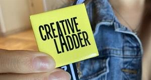 A hand holds a square button displaying the Creative Ladder logo